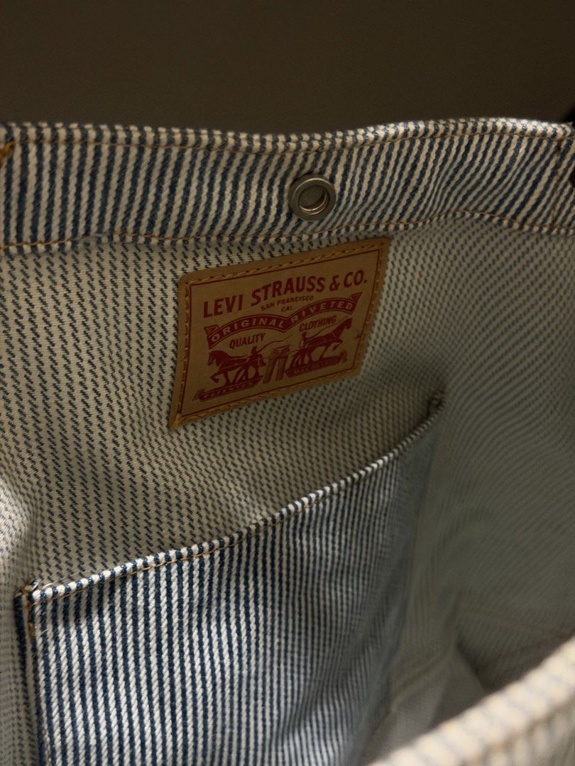 Levi's Striped Denim Tote Bag (Category: Tote Bags) located in Iloilo. Submitted by juca.sale (Listing ID 1463877787, Image 3). Description: - Classic Levi's tote bag - Blue and white pinstripe denim material - Black leather straps - Multiple exterior pockets for easy access - Interior pocket with branded Levi's tag - Spacious and durable design - Perfect for everyday use or travel.
