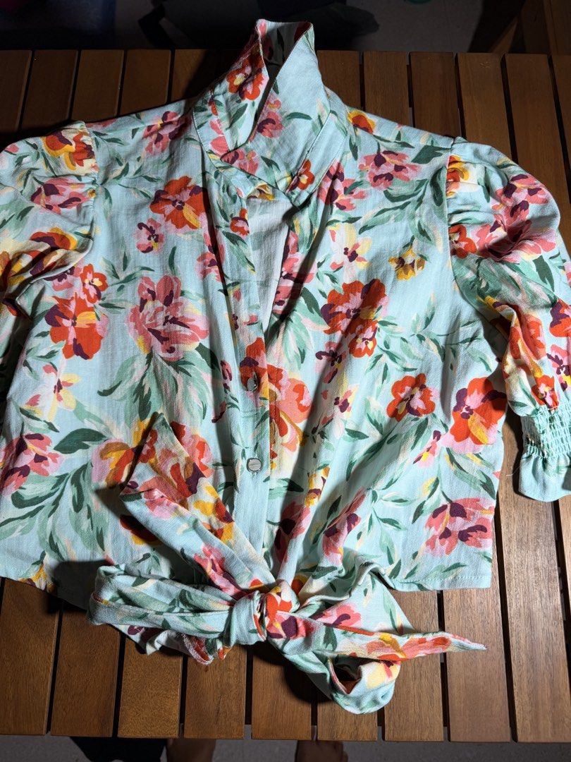 Light Blue Floral Tie-Front Blouse (Category: Blouses) located in Tuguegarao City. Submitted by joysmithznjo (Listing ID 1463746656, Image 1). Description: - Light blue blouse with vibrant floral print - Tie-front detail at the hem - Smocked cuffs - Button-up front - High collar - Lightweight fabric - Versatile: pairs well with jeans or skirts.