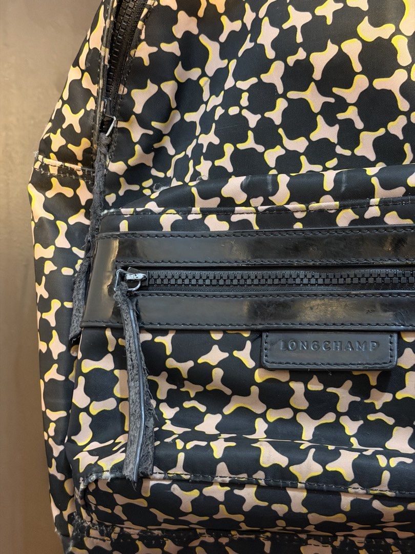 Longchamp Backpack (Category: Backpacks) located in Manila. Submitted by jlcvinci (Listing ID 1463879939, Image 2). Description: - Stylish camo print backpack from Longchamp - Color: Black, beige, and yellow pattern - Features a front zip pocket with leather trim - Note: Zipper pull on front pocket is slightly worn - Fraying on side seam near zipper - Still a functional and great bag for daily use.