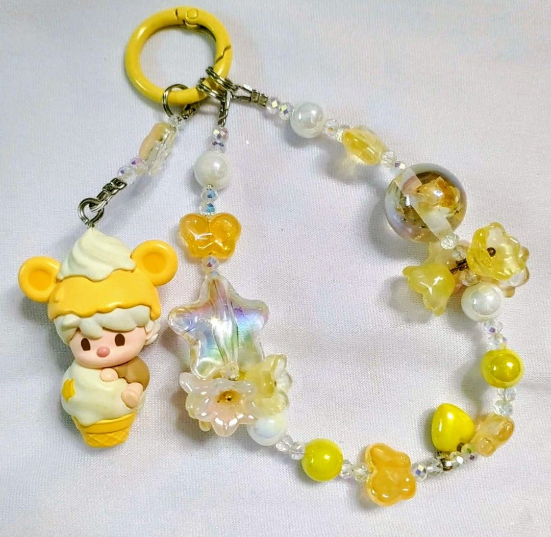 Popmart hacipupu popbean DIY charm (Category: Charms) located in Caloocan City. Submitted by jark_moonshop (Listing ID 1463860054, Image 1). Description: - Adorable ice cream bear charm - Features a beaded chain - Accented with yellow and iridescent details - Includes star, butterfly, and flower charms - Comes with a yellow ring for easy attachment to bags or keys - Perfect for decorating backpacks and purses - Unique, handmade accessory.