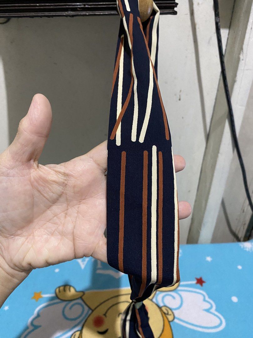 Striped Twilly Scarf with Gold Ring Accent (Category: Scarves) located in Manila. Submitted by resi.diaz (Listing ID 1463840551, Image 2). Description: - Navy blue scarf - Vertical stripes in white and brown - Includes a gold-tone ring for tying - Smooth, comfortable fabric - Versatile accessory for various styling options - Perfect for completing any outfit.