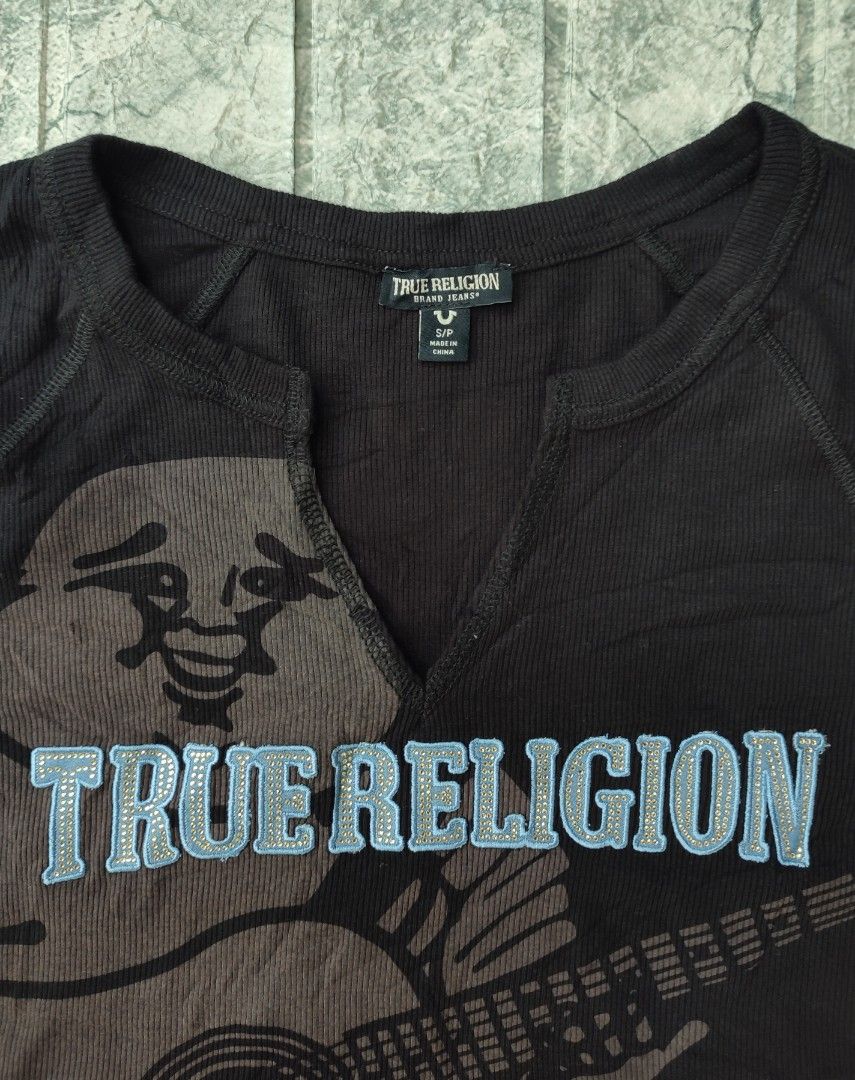 True Religion Crystal Buddha Notch Tee (Category: Sleeveless) located in Bayambang. Submitted by mon10192816 (Listing ID 1463751779, Image 3). Description: - Width 17 - Length 16 - True Religion cropped t-shirt - Features a Buddha and guitar graphic - Rhinestone details on 'True Religion' text - Notch neckline - Short sleeves - Material: Polyester, Rayon, Spandex blend - Perfect for a casual, edgy style.