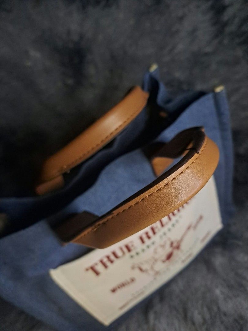 True Religion Medium Buddha Pocket Tote (Category: Luxury Bags & Wallets) located in Quezon City. Submitted by yaseen73 (Listing ID 1463927236, Image 2). Description: - Blue Denim Body With a Contrast Cream Colored Front Slip Pocket - Three Way Tote Bag Features the Iconic True Religion Logo and World Tour / Fashion for the Senses Lettering - Equipped With Structured Brown Top Handles and Typically Includes an Optional Adjustable Crossbody Strap 