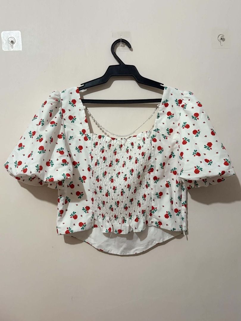White Rose Print Puff Sleeve Square Neck Top (Category: Blouses) located in San Leonardo. Submitted by burgossanleonardo.12345 (Listing ID 1463868258, Image 2). Description: - Adorable white cropped top - Features a charming red rose print - Stylish puff sleeves - Elegant square neckline - Flattering smocked detail on the front bodice - Functional button details down the front - Perfect for pairing with high-waisted jeans or skirts.