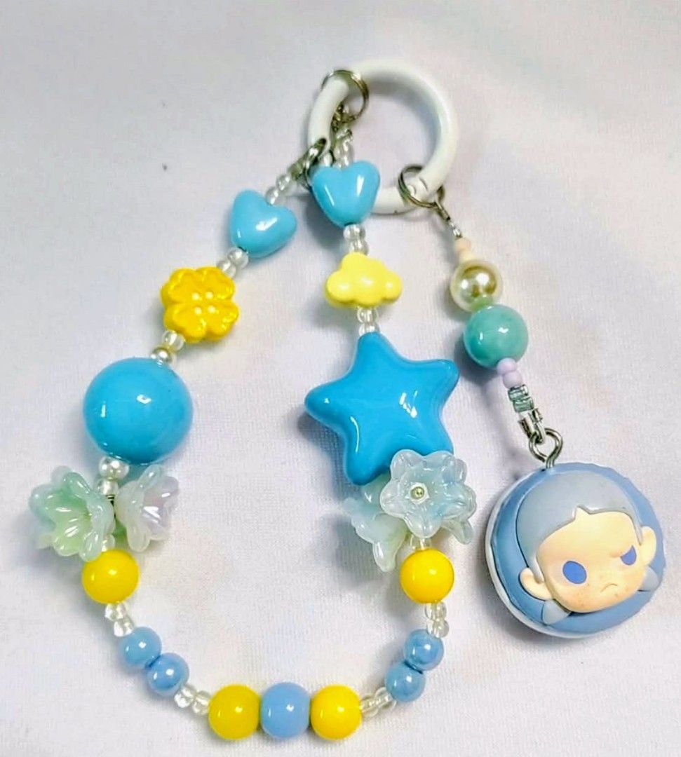 Zsiga popmart popbeans DIY charm (Category: Charms) located in Caloocan City. Submitted by jark_moonshop (Listing ID 1463843374, Image 1). Description: - Handmade beaded keychain - Features blue and yellow beads - Adorned with star, heart, and flower charms - Includes a cute, grumpy character charm - Comes with a white ring for easy attachment - Ideal accessory for bags or keys - A unique and eye-catching piece.