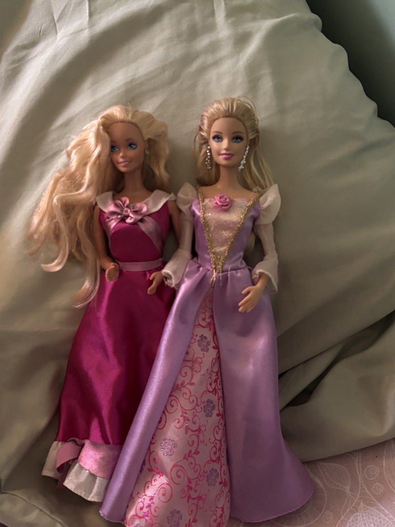 2 Barbie Dolls Princess Dresses (Category: Kids Toys) located in La Trinidad. Submitted by caicai1926 (Listing ID 1464013927, Image 1). Description: - Two beautiful Barbie princess dolls - Both have blonde hair and blue eyes - Doll 1: Pink princess gown with bow detail - Doll 2: Purple and pink satin gown with gold trim and rose accent - Includes matching shoes for both dolls.