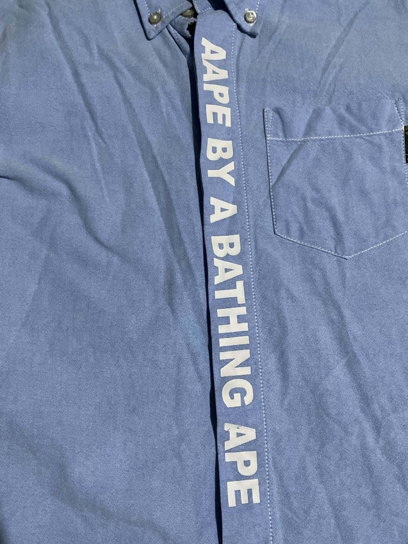 AAPE BY A BATHING APE Oxford Button-Up Shirt (Category: Tshirts & Polo Shirts ) located in Manila. Submitted by mikeee03 (Listing ID 1464117407, Image 2). Description: - Brand: AAPE BY A BATHING APE - Color: Light Blue - Style: Oxford Shirt - Size: S on tag, but fit to medium - Features: Vertical logo print on placket, logo on chest pocket, camouflage print collar lining - Occasion: Casual or smart-casual wear - All details nandyan na.