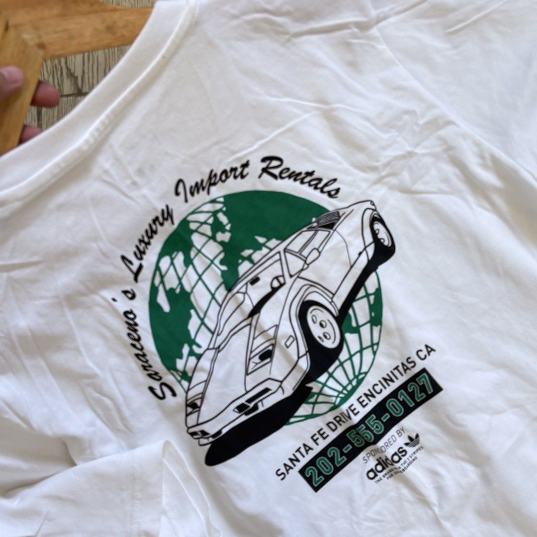 Adidas Graphic Shirt (Category: Tshirts & Polo Shirts ) located in Imus. Submitted by reloved.nd (Listing ID 1464072711, Image 2). Description: - White Adidas T-shirt - Cool vintage car graphic on the back - Text: 'Saraceno's Luxury Import Rentals', 'Santa Fe Drive Encinitas CA', and phone number - Small Adidas logo on the front chest - Ideal for casual wear.