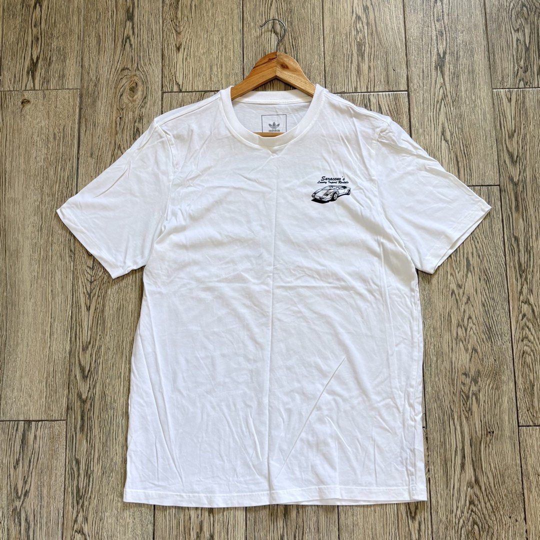 Adidas Graphic Shirt (Category: Tshirts & Polo Shirts ) located in Imus. Submitted by reloved.nd (Listing ID 1464072711, Image 1). Description: - White Adidas T-shirt - Cool vintage car graphic on the back - Text: 'Saraceno's Luxury Import Rentals', 'Santa Fe Drive Encinitas CA', and phone number - Small Adidas logo on the front chest - Ideal for casual wear.