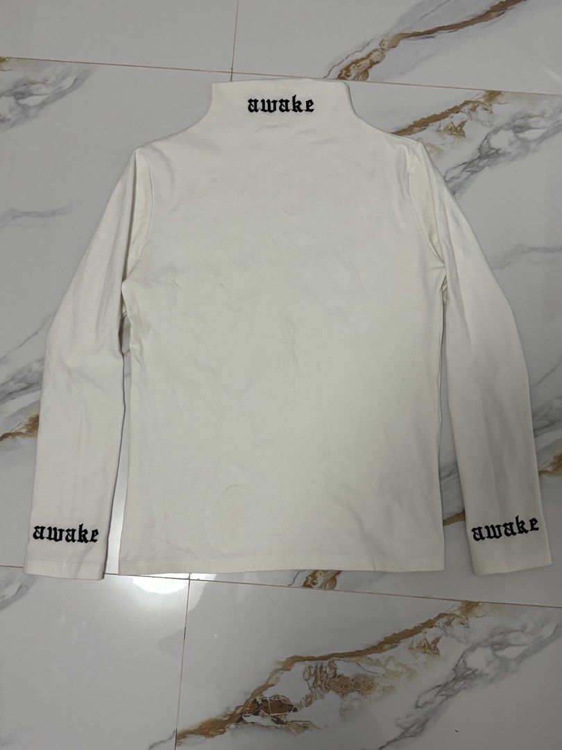 AWAKE White Turtleneck Long Sleeve Top (Category: Longsleeves) located in Silang. Submitted by lakasthrift1577 (Listing ID 1464028647, Image 1). Description: - White long sleeve turtleneck top - Features 'awake' embroidery on collar and sleeves - Made of 100% cotton - Brand: AYURA - Versatile for layering or standalone wear - Simple and stylish design -issue cut main tag Awake -Fresh condition,authentic .