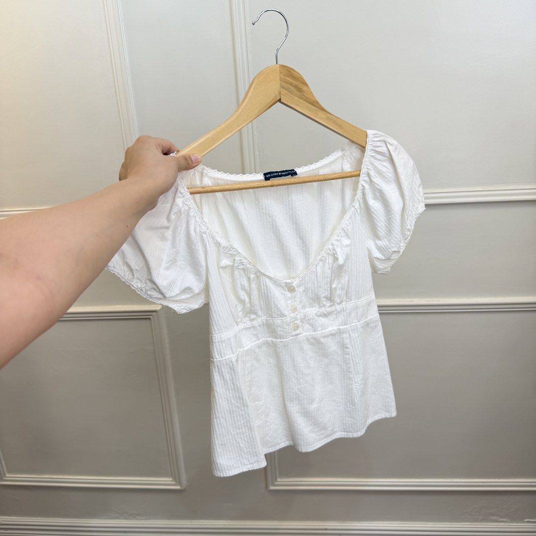 Brandy Melville White Puff Sleeve Square Neck Top (Category: Blouses) located in Manila. Submitted by angelll0123 (Listing ID 1463970843, Image 1). Description: - Can fit small-medium - White Brandy Melville top - Features puff sleeves and a square neckline - Button details down the front - Textured fabric for a unique feel - Versatile piece, great for casual styling with jeans or skirts.