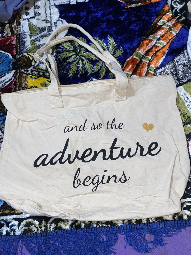 Canvas Tote Bag "Adventure Begins" (Category: Tote Bags) located in Manila. Submitted by reginemarquez412 (Listing ID 1464055201, Image 1). Description: - Cream canvas tote bag - Features 'and so the adventure begins' print - Adorned with a small gold heart detail - Secure zipper closure - Ideal for everyday use or travel - Spacious interior.