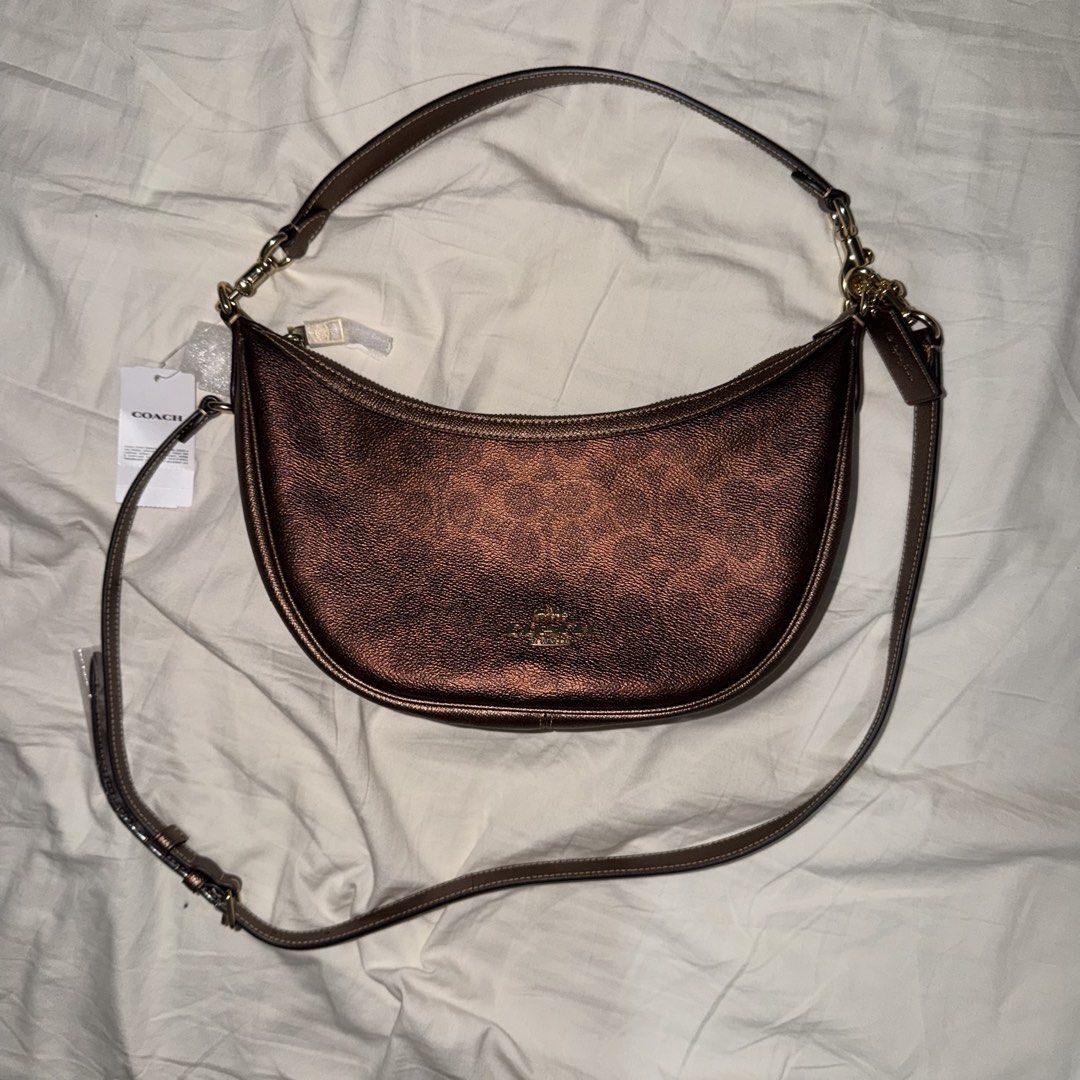 Coach Metallic Brown Copper Aria Half Moon Shoulder Bag (Category: Shoulder Bags) located in Caloocan City. Submitted by dearvals (Listing ID 1463966899, Image 1). Description: - Coach crescent shoulder bag - Metallic brown with subtle texture - Gold hardware and front Coach logo - Adjustable strap - Brand new with original tags attached - Versatile for everyday or evening wear.
