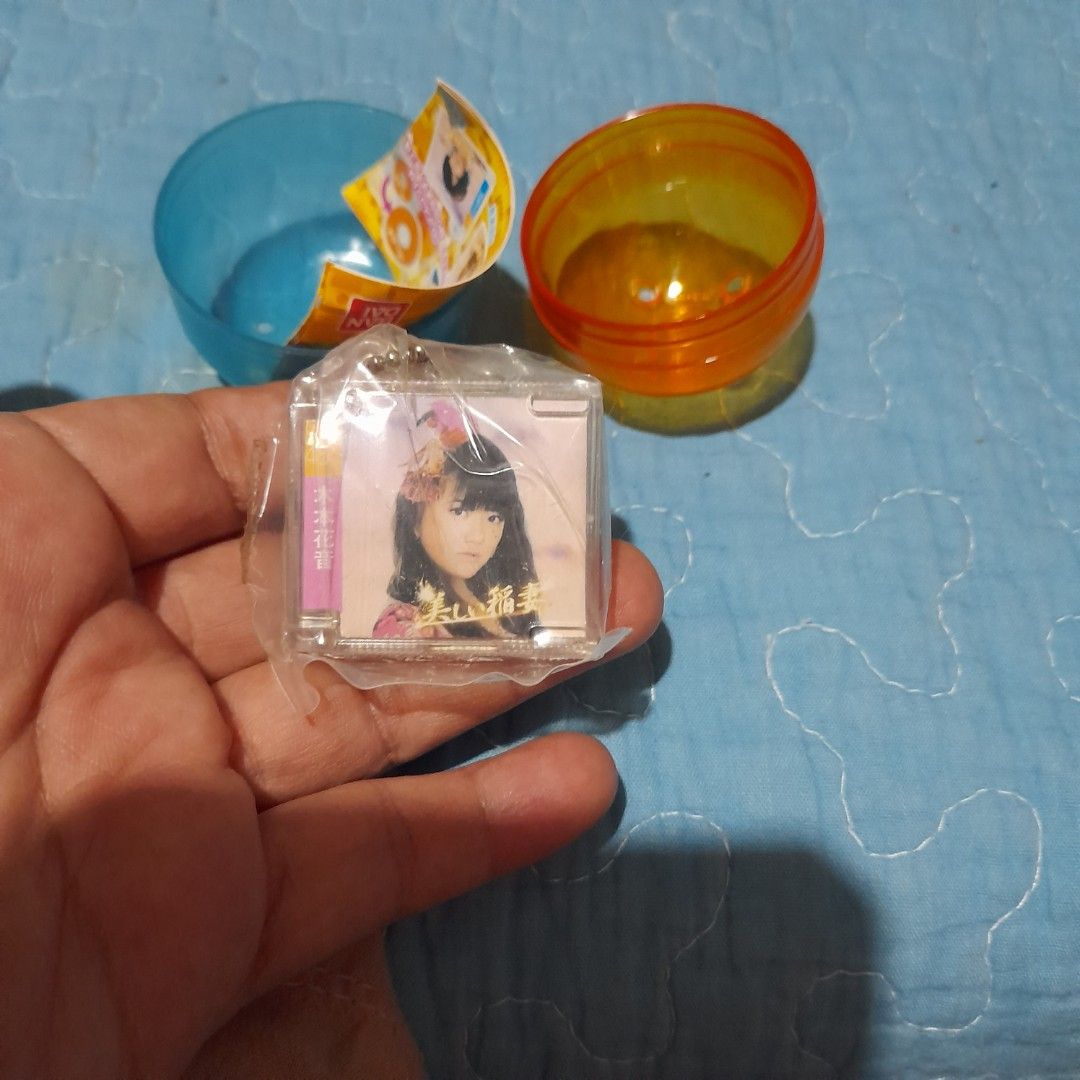 Gachapon Capsule Toy with Mini CD Keychain (Category: Designer & Blind Box Toys) located in Bocaue. Submitted by marajapansurplus (Listing ID 1464018896, Image 2). Description: - Authentic Gachapon capsule toy - Includes a mini CD with Japanese text - Features a keychain with a girl's picture - Original orange and blue capsule packaging - Sold as is.