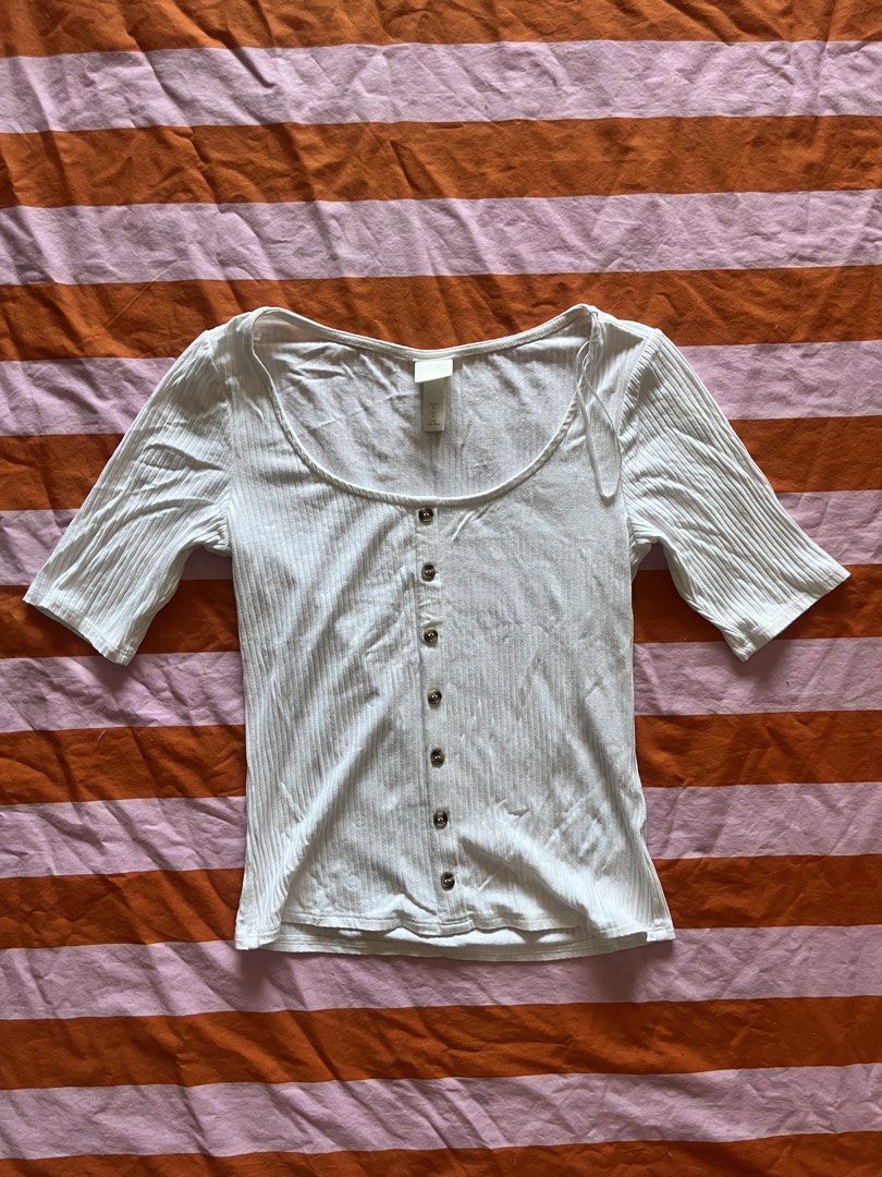 H&M White Ribbed Button-Up Short Sleeve Top (Category: Shirts) located in Mandaluyong City. Submitted by hopeworldplane (Listing ID 1463959223, Image 1). Description: - White ribbed top from H&M - Short sleeves - Scoop neckline - Button-up front with brown buttons - Very stretchy material - Perfect for pairing with jeans or skirts - Easy to dress up or down.
