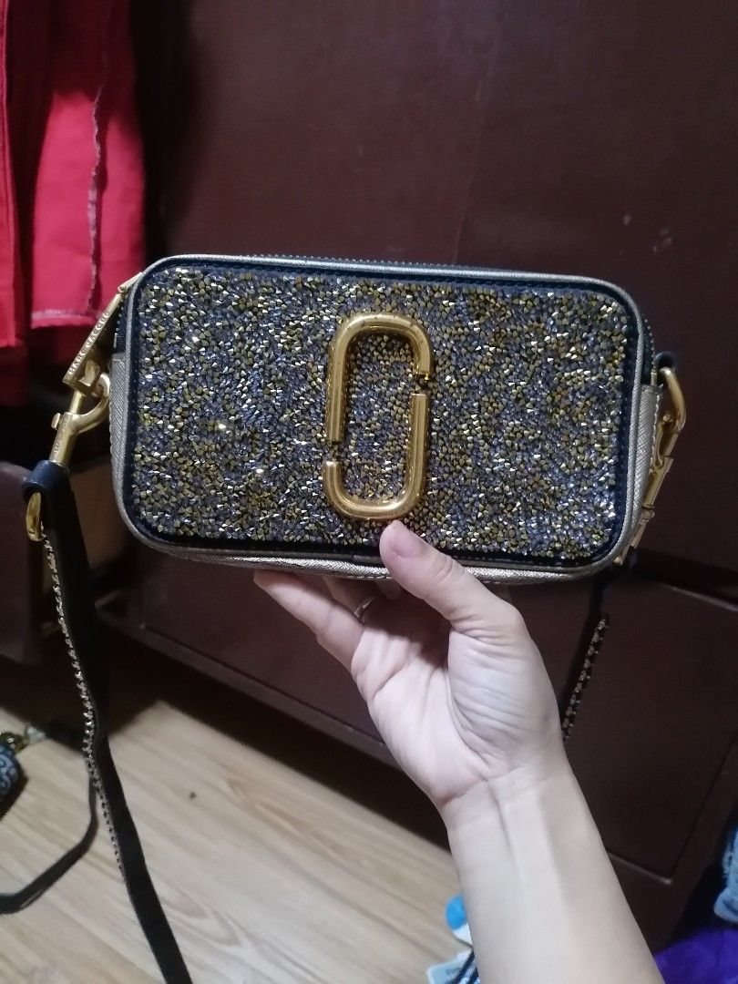 Marc Jacobs Glitter Camera Bag (Category: Luxury Bags & Wallets) located in Digos. Submitted by crodualady82694 (Listing ID 1463983920, Image 1). Description: - Brand: Marc Jacobs - Color: Black with all-over gold glitter - Hardware: Signature double J logo - Closure: Zip - Strap: Detachable crossbody strap - Origin: Made in China - Style: Perfect for nights out or adding a touch of sparkle to any outfit.