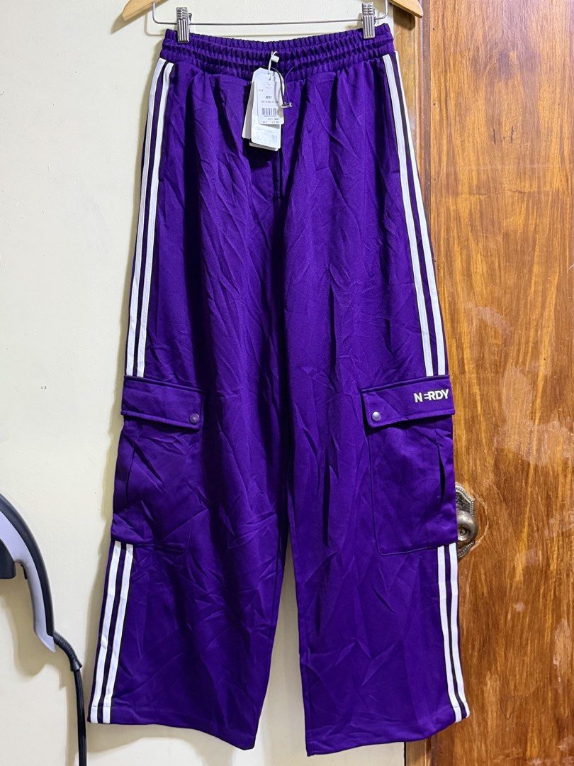 Nerdy Purple Cargo Track Pants (Category: Joggers) located in Paete. Submitted by skydruemadison (Listing ID 1464044192, Image 1). Description: - Brand: Nerdy - Color: Purple - Style: Cargo track pants - Features: Classic three stripes down the side, Nerdy logo on pocket - Waistband: Elastic with drawstring - Pockets: Front, back, and two cargo pockets on legs - Ideal for: Casual wear, lounging.