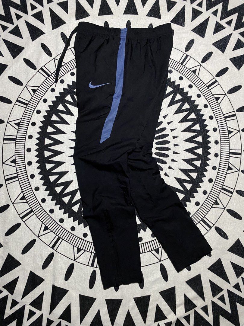 Nike Dri-FIT Black Track Pants (Category: Joggers) located in Badiangan. Submitted by iralorana.thrift (Listing ID 1463960273, Image 1). Description: - Black Nike track pants - Blue accent details - Iconic Nike Swoosh logo - Dri-FIT technology for moisture-wicking - Comfortable elastic waistband with drawstring - Zippers at the ankle for adjustable fit - Ideal for athletic activities or everyday casual wear.