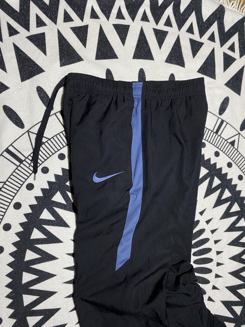 Nike Dri-FIT Black Track Pants (Category: Joggers) located in Badiangan. Submitted by iralorana.thrift (Listing ID 1463960273, Image 2). Description: - Black Nike track pants - Blue accent details - Iconic Nike Swoosh logo - Dri-FIT technology for moisture-wicking - Comfortable elastic waistband with drawstring - Zippers at the ankle for adjustable fit - Ideal for athletic activities or everyday casual wear.