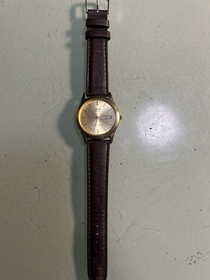 Q&Q Quartz Watch with Leather Strap (Category: Men's Watches) located in Cavite. Submitted by mamamia73 (Listing ID 1464036996, Image 2). Description: - Gold-tone analog watch - Displays day and date - Water resistant - Brown leather strap (shows some wear) - Works well - Ideal for everyday wear.