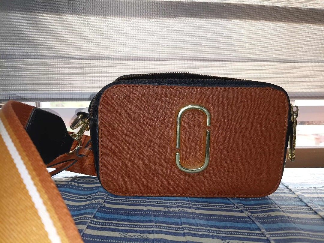 The Snapshot Camera Bag by Marc Jacobs (Category: Cross-body Bags) located in Manila. Submitted by keenphoenix_9ed053 (Listing ID 1464047557, Image 1). Description: - Brown crossbody bag - Gold 'O' logo detail - Secure zipper closure - Adjustable strap with orange and white stripes - Ideal size for everyday essentials.