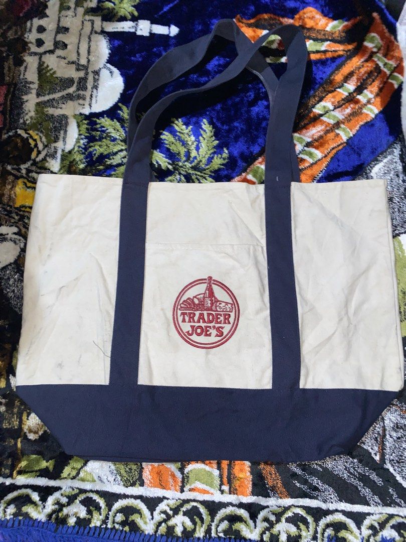 Trader Joe's Canvas Tote Bag (Category: Tote Bags) located in Manila. Submitted by reginemarquez412 (Listing ID 1464057015, Image 1). Description: - Classic Trader Joe's canvas tote bag - Cream color with navy blue trim and handles - Features iconic Trader Joe's logo on front pocket - Ideal for groceries or everyday use - Durable and reusable design.
