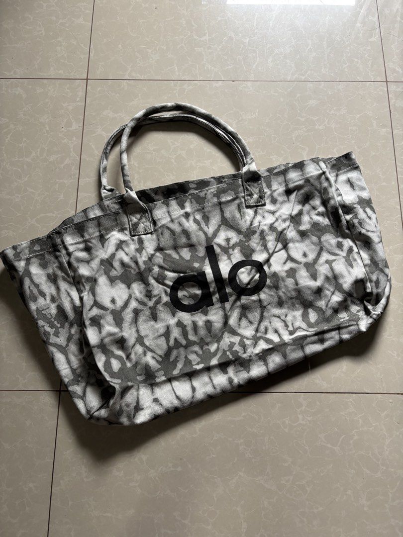 Alo Tote Bag Tie-Dye Print (Category: Tote Bags) located in Quezon City. Submitted by nojthrift (Listing ID 1464252530, Image 1). Description: - Stylish tie-dye print Alo tote bag - Features a black 'alo' logo on the front - Durable canvas material - One size fits all - Ideal for everyday use, gym sessions, or beach outings - Offers ample interior space.