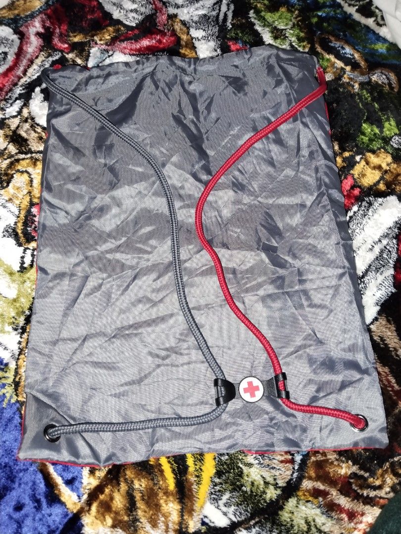 American Red Cross Drawstring Backpack (Category: Backpacks) located in Mabalacat. Submitted by al_amin_thrift (Listing ID 1464227454, Image 3). Description: 🎒 American Red Cross Drawstring Backpack Item Details - Front: Bright red with official white Red Cross logo + "American Red Cross" lettering ​ - Back: Sleek dark gray / charcoal ​ - Straps: Dual drawstring — one red, one gray — doubles as shoulder straps ​ - Material: Lightweight, smooth, 