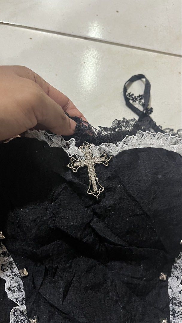 Black Lace Corset Top with Cross Charm (Category: Sleeveless) located in Valencia. Submitted by thriftyfinds01 (Listing ID 1464168039, Image 3). Description: - Black corset top - White lace trim - Silver stud details on front - Adjustable straps - Small cross charm attached at bust - Versatile for layering or standalone wear - Unique gothic-inspired design.