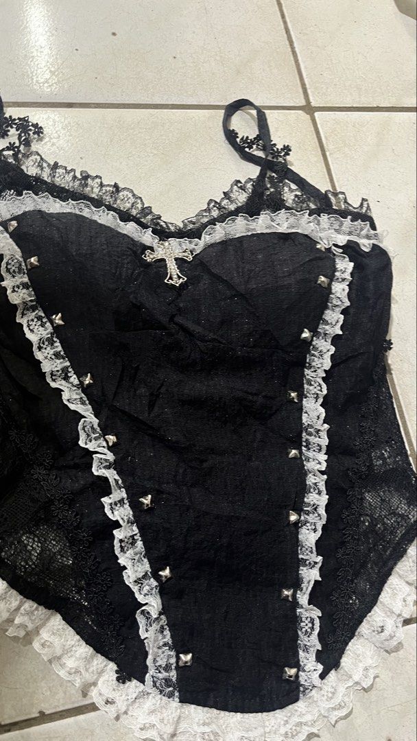 Black Lace Corset Top with Cross Charm (Category: Sleeveless) located in Valencia. Submitted by thriftyfinds01 (Listing ID 1464168039, Image 2). Description: - Black corset top - White lace trim - Silver stud details on front - Adjustable straps - Small cross charm attached at bust - Versatile for layering or standalone wear - Unique gothic-inspired design.
