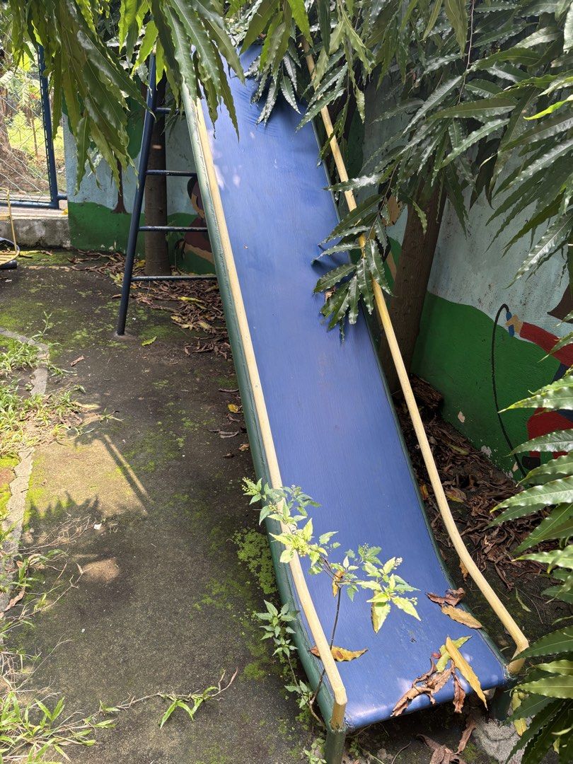 Blue Metal Playground Slide with Ladder (Category: Kids Toys) located in Paranaque City. Submitted by lilovpb (Listing ID 1464173146, Image 1). Description: - Blue metal slide with vibrant yellow and green trim. - Sturdy metal ladder with blue and red supports. - Shows some signs of rust and wear, adding character. - Ideal for enhancing any backyard or play area. - Requires a bit of cleaning and touch-up for a fresh look..