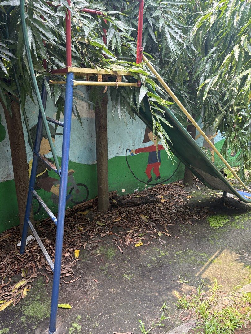 Blue Metal Playground Slide with Ladder (Category: Kids Toys) located in Paranaque City. Submitted by lilovpb (Listing ID 1464173146, Image 2). Description: - Blue metal slide with vibrant yellow and green trim. - Sturdy metal ladder with blue and red supports. - Shows some signs of rust and wear, adding character. - Ideal for enhancing any backyard or play area. - Requires a bit of cleaning and touch-up for a fresh look..