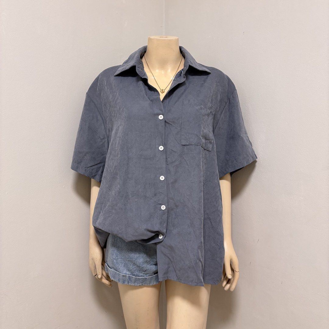 Blue Short Sleeve Buttondown Polo (Category: Blouses) located in Imus. Submitted by reloved.nd (Listing ID 1464261029, Image 1). Description: - Grey short sleeve button-up shirt - Left chest pocket - Fabric has a slightly crinkled texture - Versatile for casual styling with shorts or jeans.