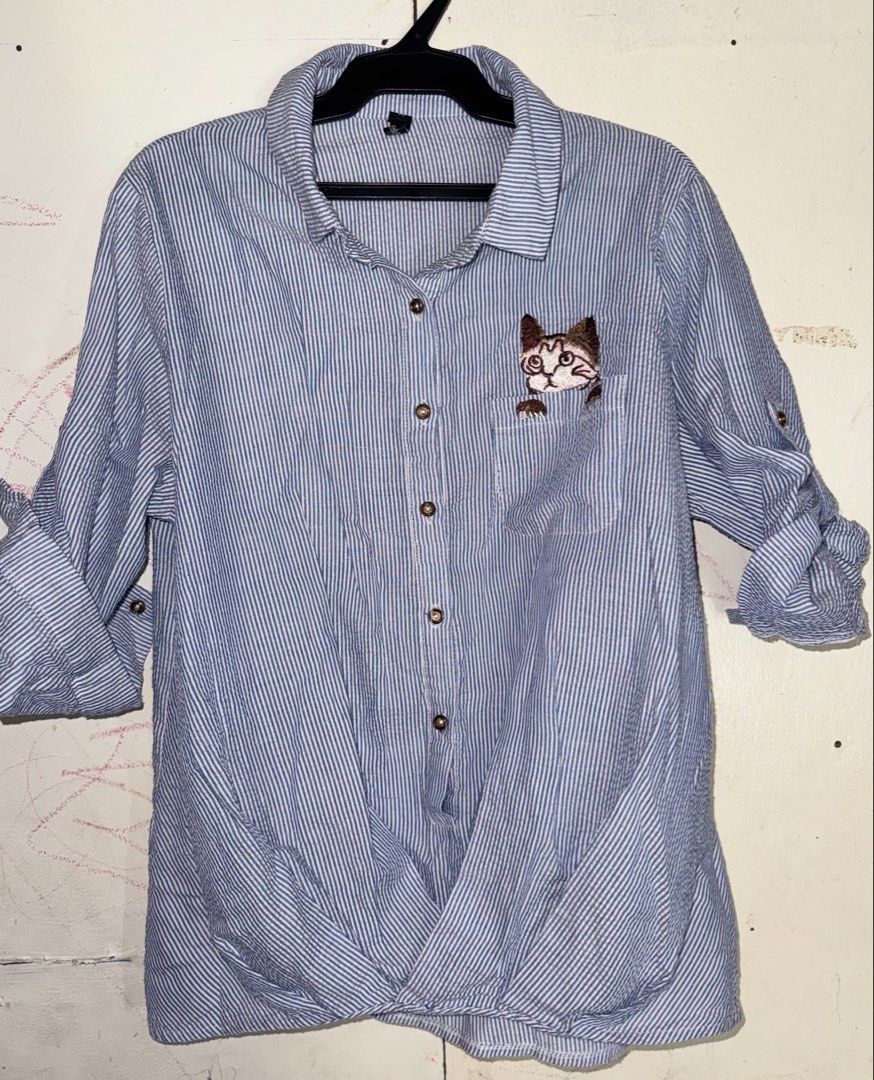 Blue Striped Shirt with Cat Embroidery (Category: Shirts) located in Santiago. Submitted by eogg30 (Listing ID 1464140713, Image 1). Description: - Adorable blue and white striped button-up shirt. - Features a cute embroidered cat peeking from the pocket. - Sleeves can be rolled up and secured with button tabs. - Stylish knot detail at the bottom hem. - Ideal for creating a relaxed, casual look..