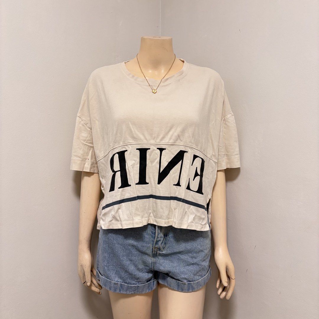 Cream Crop Top (Category: Shirts) located in Imus. Submitted by reloved.nd (Listing ID 1464261042, Image 1). Description: - Cream colored cropped t-shirt - Features a bold black graphic print on the front - Short sleeves - Relaxed fit - Versatile for casual styling with denim shorts or jeans.