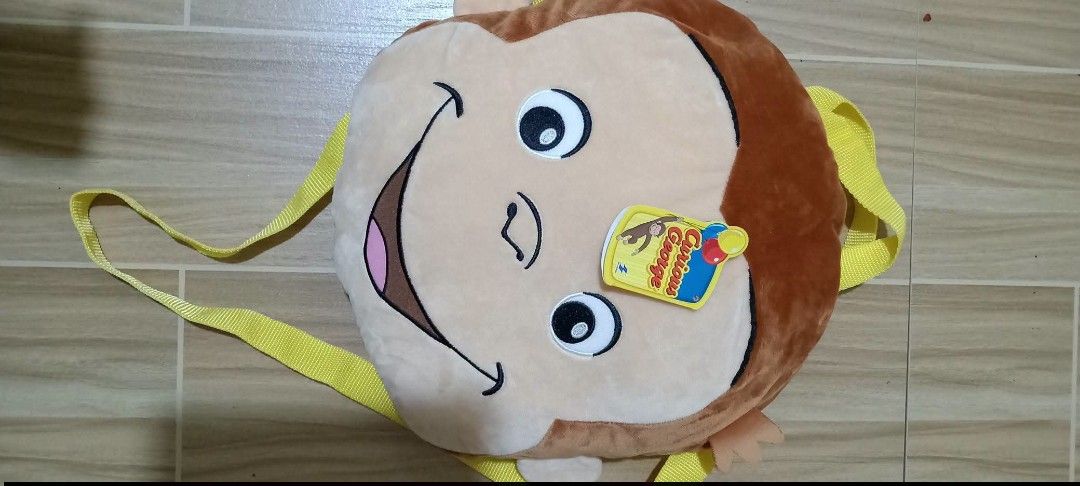 Curious George Plush Backpack Bag (Category: Plushies & Soft Toys) located in Gapan. Submitted by montesnora80204 (Listing ID 1464351218, Image 1). Description: - Adorable Curious George plush backpack - Features character's face on the front - "Curious George" name printed on the back - Lined with yellow satin inside - Secure clasp closure - Adjustable yellow straps - Ideal for children or Curious George enthusiasts.