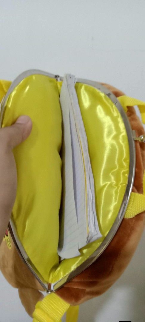 Curious George Plush Backpack Bag (Category: Plushies & Soft Toys) located in Gapan. Submitted by montesnora80204 (Listing ID 1464351218, Image 3). Description: - Adorable Curious George plush backpack - Features character's face on the front - "Curious George" name printed on the back - Lined with yellow satin inside - Secure clasp closure - Adjustable yellow straps - Ideal for children or Curious George enthusiasts.