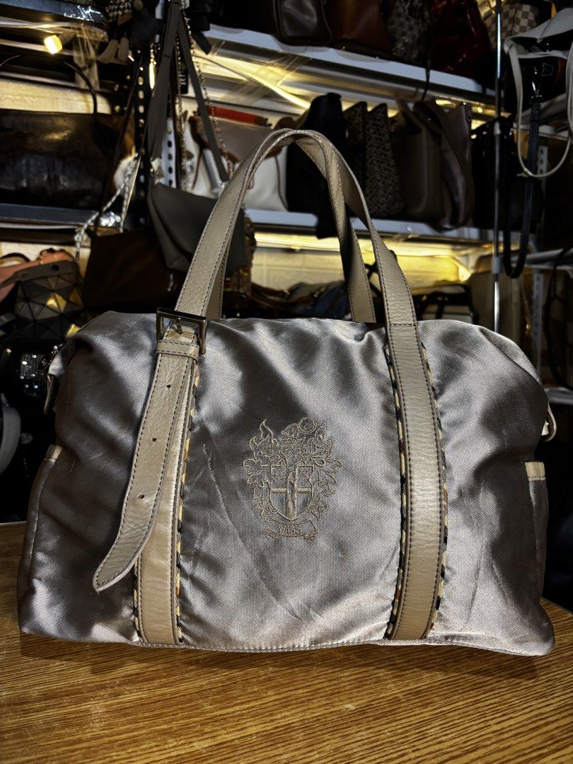 DAKS Silver Nylon Leather Trim Duffle Bag (Category: Luxury Bags & Wallets) located in Caloocan City. Submitted by _avionlineshop24 (Listing ID 1464138192, Image 1). Description: - Stylish silver duffle bag by DAKS - Accented with elegant tan leather trim - Iconic DAKS crest embroidered on the front - Secure zipper closure with a convenient leather pull tab - Practical side pockets for easy access - Ideal for weekend getaways or everyday adventur