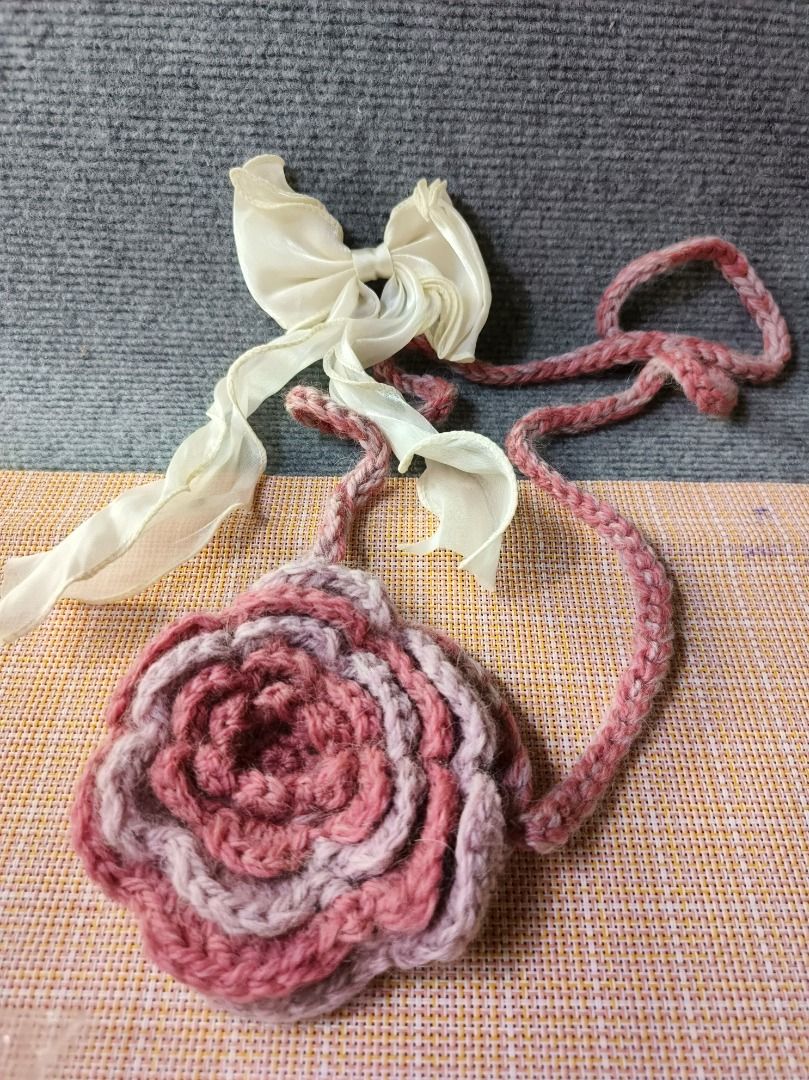 Handmade Crocheted Rose Bag with Ribbon (Category: Shoulder Bags) located in San Leonardo. Submitted by burgossanleonardo.12345 (Listing ID 1464182115, Image 1). Description: - Cute crocheted bag shaped like a rose. - Made with pink and white yarn. - Features a braided strap. - Adorned with a delicate cream ribbon bow. - Small size, perfect for coins or small trinkets. - Unique, handmade item. - Great for gifting or personal use..