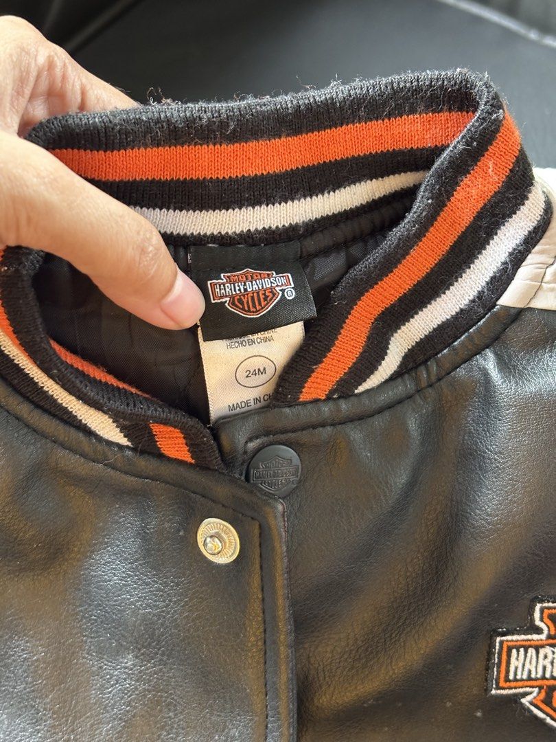 Harley-Davidson Baby Varsity Jacket 24M (Category: Babies & Kids Fashion) located in Mati. Submitted by sharieeng (Listing ID 1464149646, Image 2). Description: - Adorable Harley-Davidson varsity jacket for kids. - Classic black body with vibrant orange and white sleeves. - Features a comfortable ribbed collar, cuffs, and hem. - Easy snap button closure for quick dressing. - Quilted lining provides extra warmth. - Ideal for any little fan of Harl