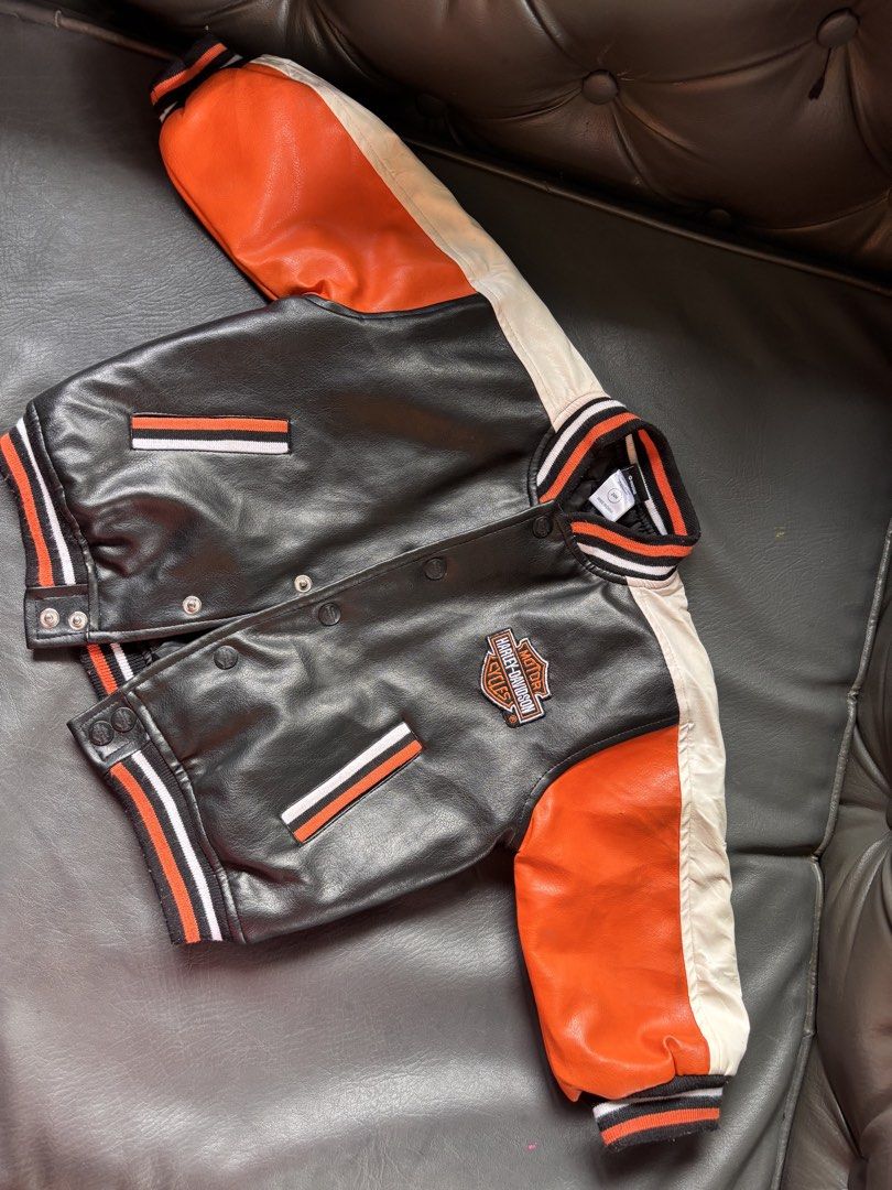 Harley-Davidson Baby Varsity Jacket 24M (Category: Babies & Kids Fashion) located in Mati. Submitted by sharieeng (Listing ID 1464149646, Image 1). Description: - Adorable Harley-Davidson varsity jacket for kids. - Classic black body with vibrant orange and white sleeves. - Features a comfortable ribbed collar, cuffs, and hem. - Easy snap button closure for quick dressing. - Quilted lining provides extra warmth. - Ideal for any little fan of Harl