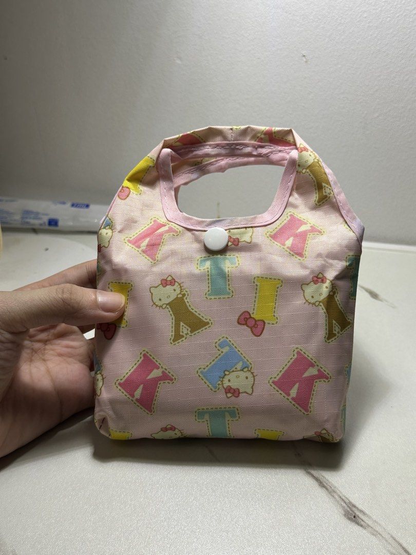 Hello Kitty Sanrio Reusable Shopping Bag (Category: Tote Bags) located in Quezon City. Submitted by swift.thriftz (Listing ID 1464316519, Image 2). Description: - Umbrella-like material - Adorable pink reusable shopping bag featuring Kitty and alphabet print. - Folds into a compact pouch for convenient storage and portability. - Ideal for grocery shopping, daily errands, and more. - Lightweight yet durable construction. - Authentic Sanrio product
