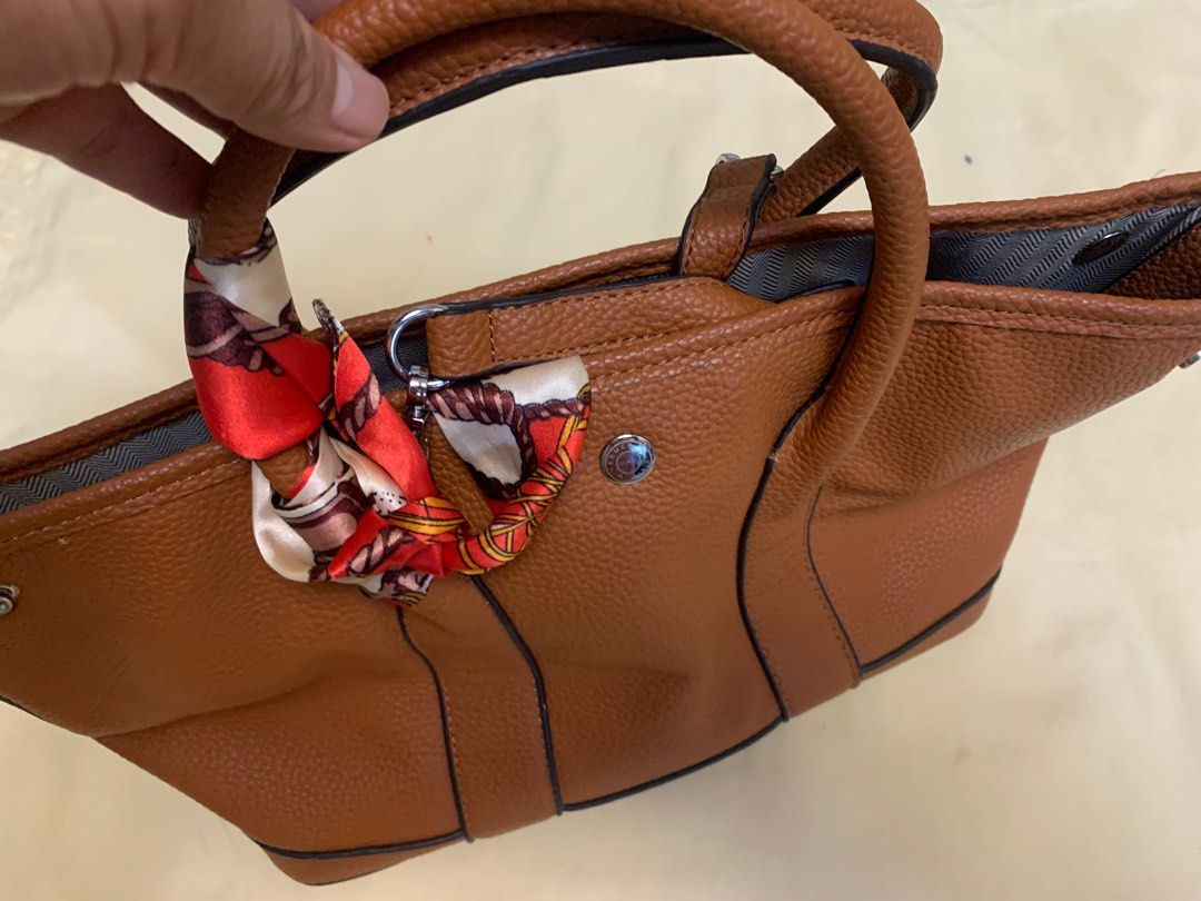 Hermes Brown Leather Handbag with Scarf Accent (Category: Shoulder Bags) located in Bulacan. Submitted by heartlove_holb (Listing ID 1464298621, Image 2). Description: - Genuine brown pebbled leather handbag - Adorned with a decorative scarf tied to the handle - Top zipper closure for security - Interior includes a zippered pocket and a slip pocket - Slip pocket features 'Hermes Paris Made in Italy' embossing - Ideal as a versatile everyday bag.