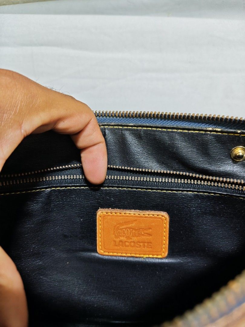 Lacoste Leather Pouch Clutch Bag (Category: Purses & Pouches) located in Isulan. Submitted by jaysthrift (Listing ID 1464225134, Image 2). Description: - Classic black and tan leather pouch by Lacoste. - Ideal size for carrying your essentials. - Secure zipper closure to keep items safe. - Interior features a small leather tag with the iconic Lacoste logo. - Convenient wrist strap attached for easy carrying. - Approximate dimensions: 9 inches wid