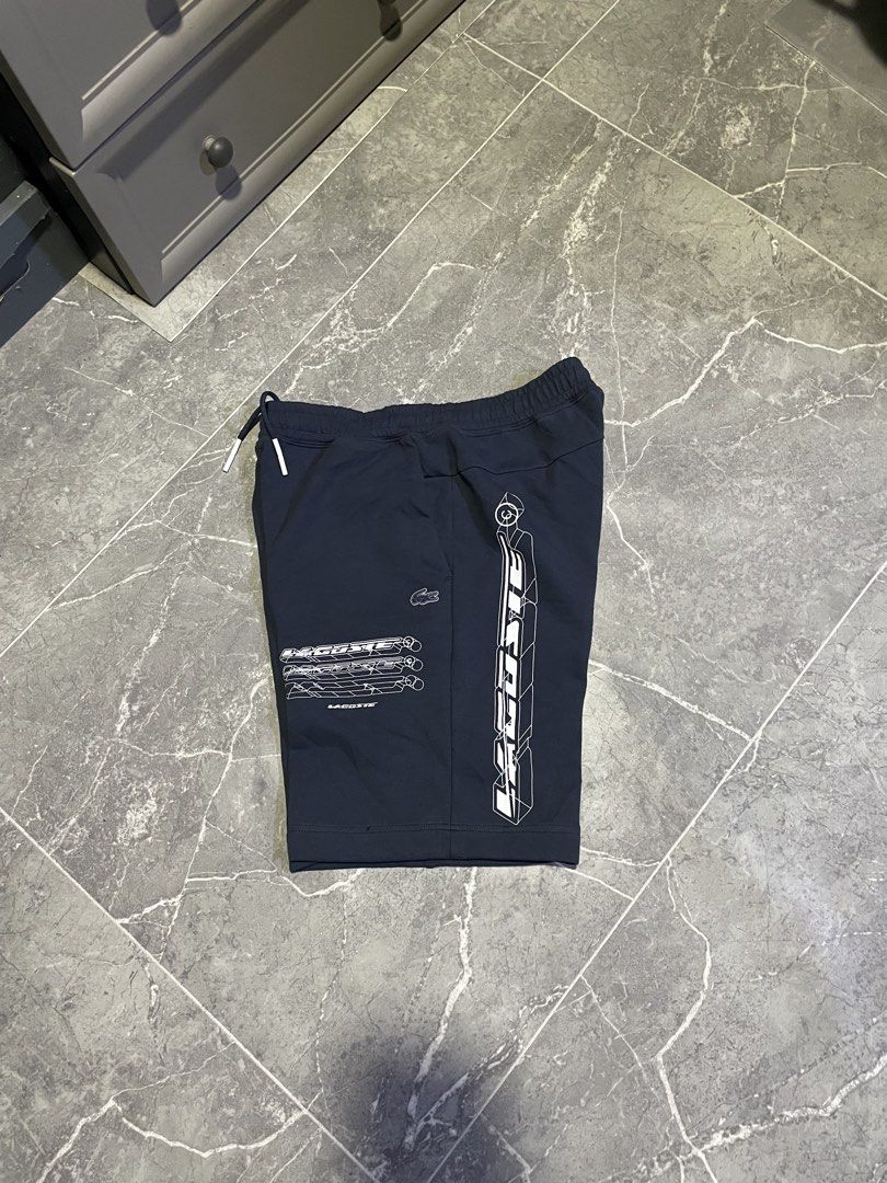 Lacoste Navy Blue Graphic Shorts (Category: Shorts) located in Buenavista. Submitted by ivoperez27 (Listing ID 1464308897, Image 1). Description: - Navy blue Lacoste shorts - Bold white graphic design on the side - Smaller graphics on the front - Elastic waistband with drawstring - Comfortable fit for everyday wear - Perfect for casual outings - 30-34 waistline - 19 length -9.7/10 colorate - issue see last picture (black dots)(minimal hairline).