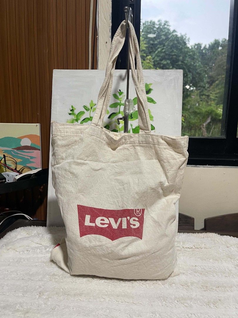 Levi's Tote Bag (Category: Tote Bags) located in Naawan. Submitted by twilly.apparel2 (Listing ID 1464217708, Image 1). Description: - Cream colored canvas tote bag - Features classic Levi's logo on one side - "NANBA 15TH ANNIVERSARY" printed in red on the other side - Drawstring closure at the top - Ideal for everyday use or as a shopping bag.