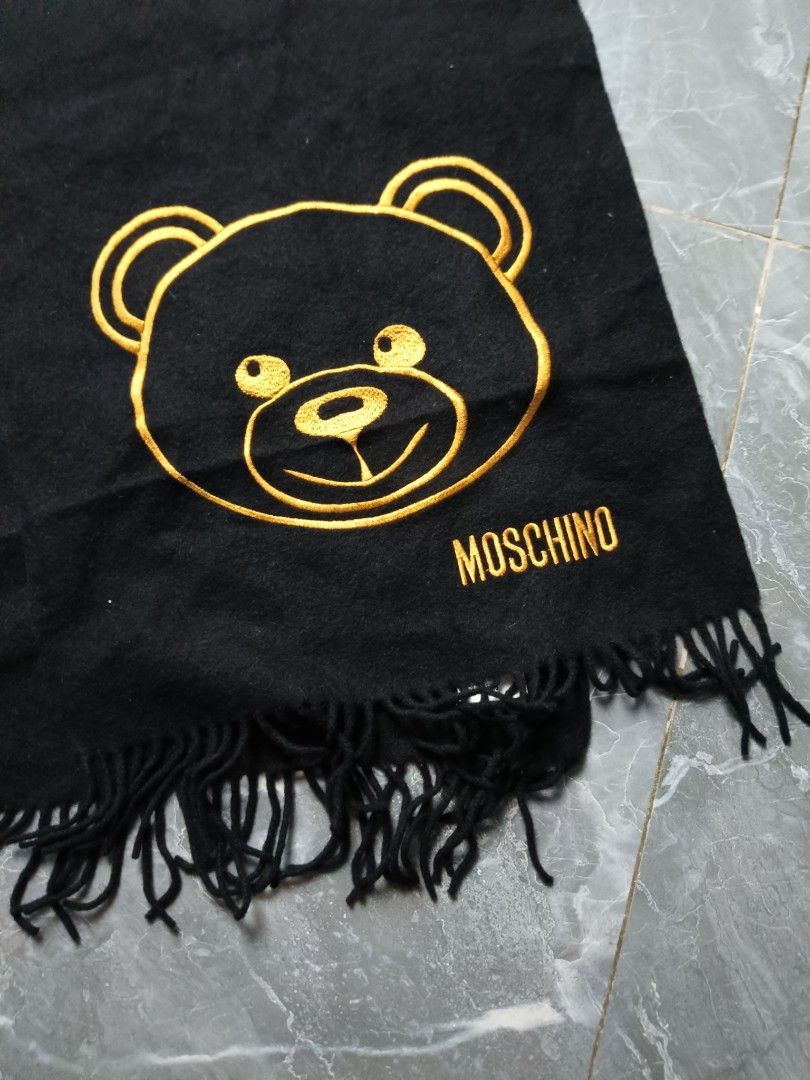 Moschino Black Teddy Bear Scarf (Category: Scarves) located in Valenzuela. Submitted by 2ndhandmarket.ph (Listing ID 1464268698, Image 2). Description: - Iconic Moschino teddy bear logo embroidered in gold - Chic black color - Soft, comfortable material - Stylish fringed edges - Perfect for warmth and fashion - Approximate dimensions: 160cm (length) x 20cm (width).