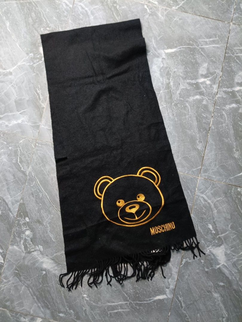 Moschino Black Teddy Bear Scarf (Category: Scarves) located in Valenzuela. Submitted by 2ndhandmarket.ph (Listing ID 1464268698, Image 1). Description: - Iconic Moschino teddy bear logo embroidered in gold - Chic black color - Soft, comfortable material - Stylish fringed edges - Perfect for warmth and fashion - Approximate dimensions: 160cm (length) x 20cm (width).