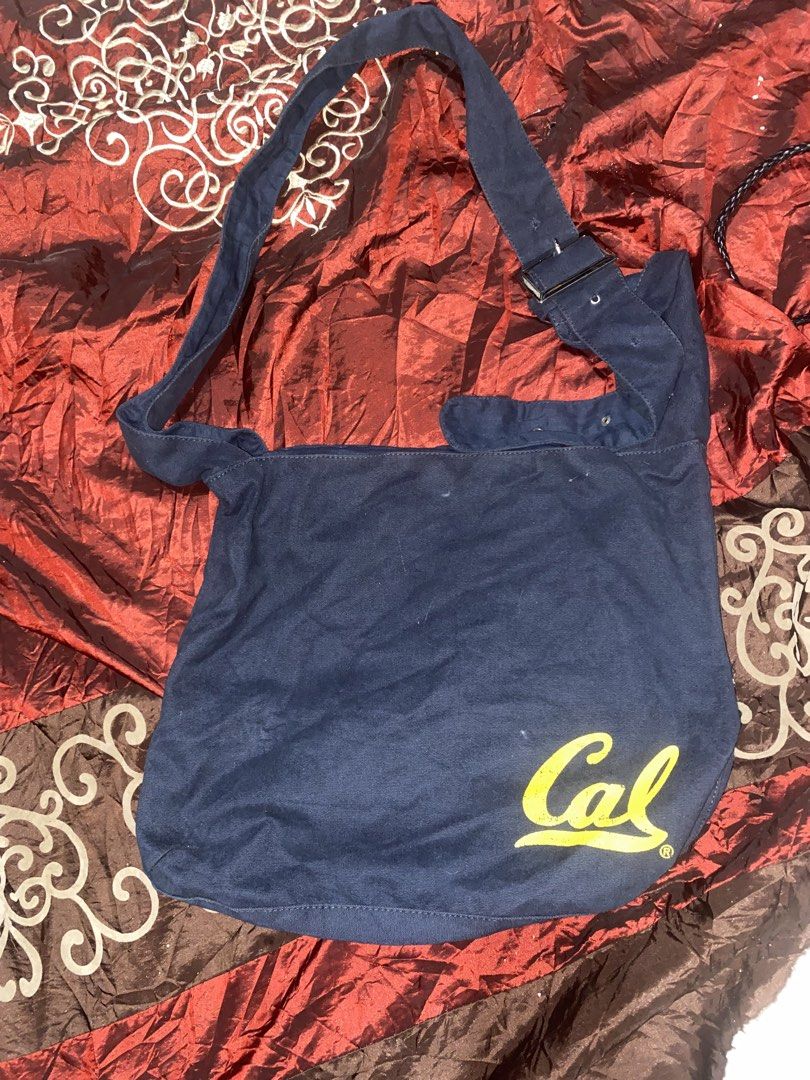 Navy Blue 'Cal' Tote Bag (Category: Tote Bags) located in Manila. Submitted by reginemarquez412 (Listing ID 1464229104, Image 2). Description: - Classic navy blue canvas tote bag - Features a yellow 'Cal' graphic - Adjustable strap with buckle for comfort - Large main compartment for ample storage - Ideal for everyday use, books, or groceries - Simple, functional, and stylish design.