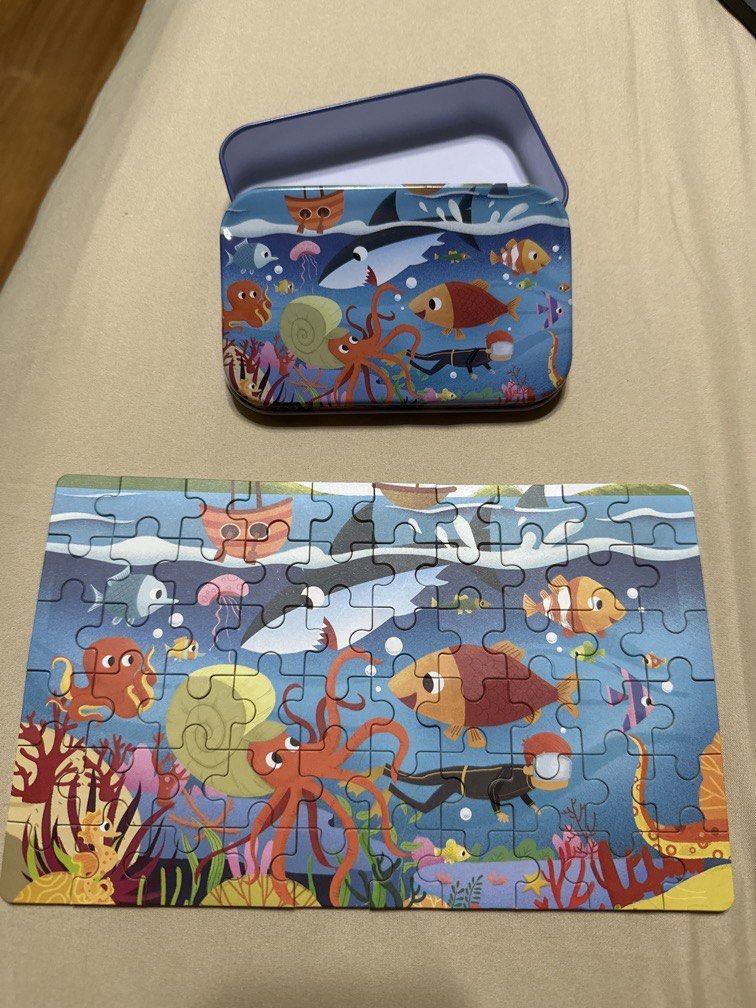 Ocean Scene Jigsaw Puzzle in Tin Box (Category: Board Games & Puzzles) located in Manila. Submitted by silver.truemountain (Listing ID 1464166363, Image 1). Description: - Fun jigsaw puzzle with a vibrant underwater scene. - Features octopuses, colorful fish, a shark, and a diver. - Comes with a cute and durable tin box for easy storage. - All puzzle pieces are accounted for and ready for assembly. - Ideal for kids and adults who enjoy puzzles. -